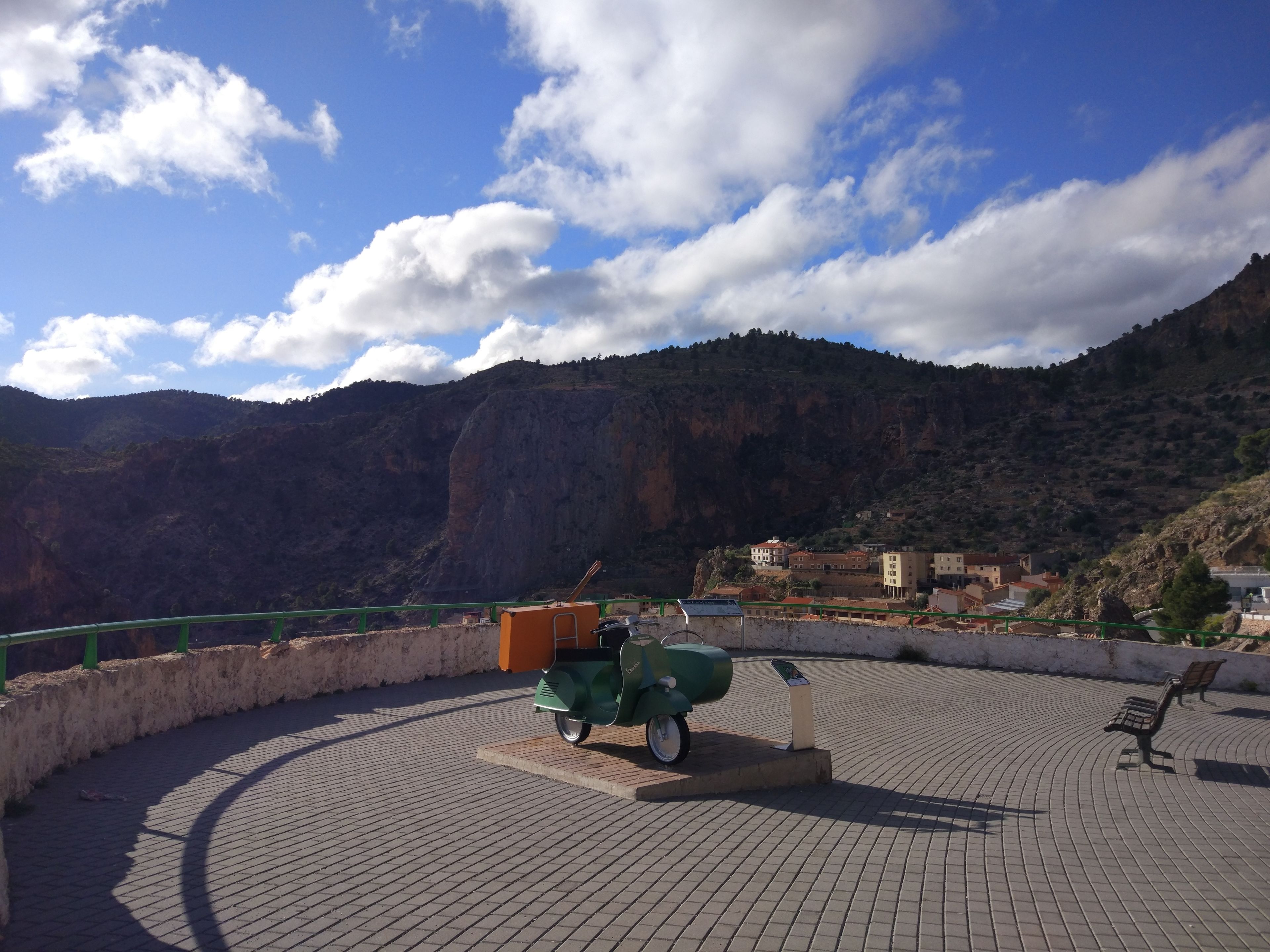 A paved area with a green scooter, a bench, and a building in the background.