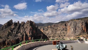 Una plataforma pavimentada con barandilla verde, con vista a un paisaje rocoso bajo un cielo despejado.