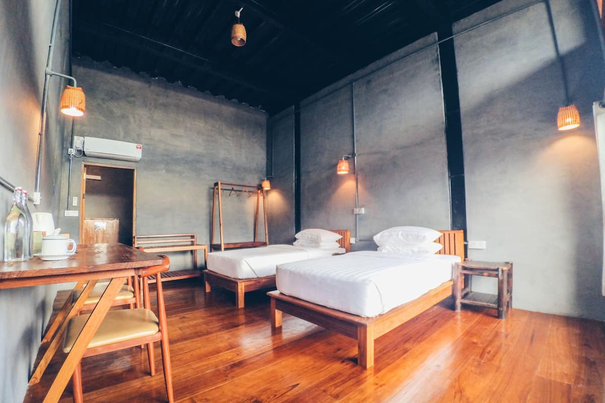 A room with two wooden beds, a wooden desk with a chair, and a small table with a bottle and cup.