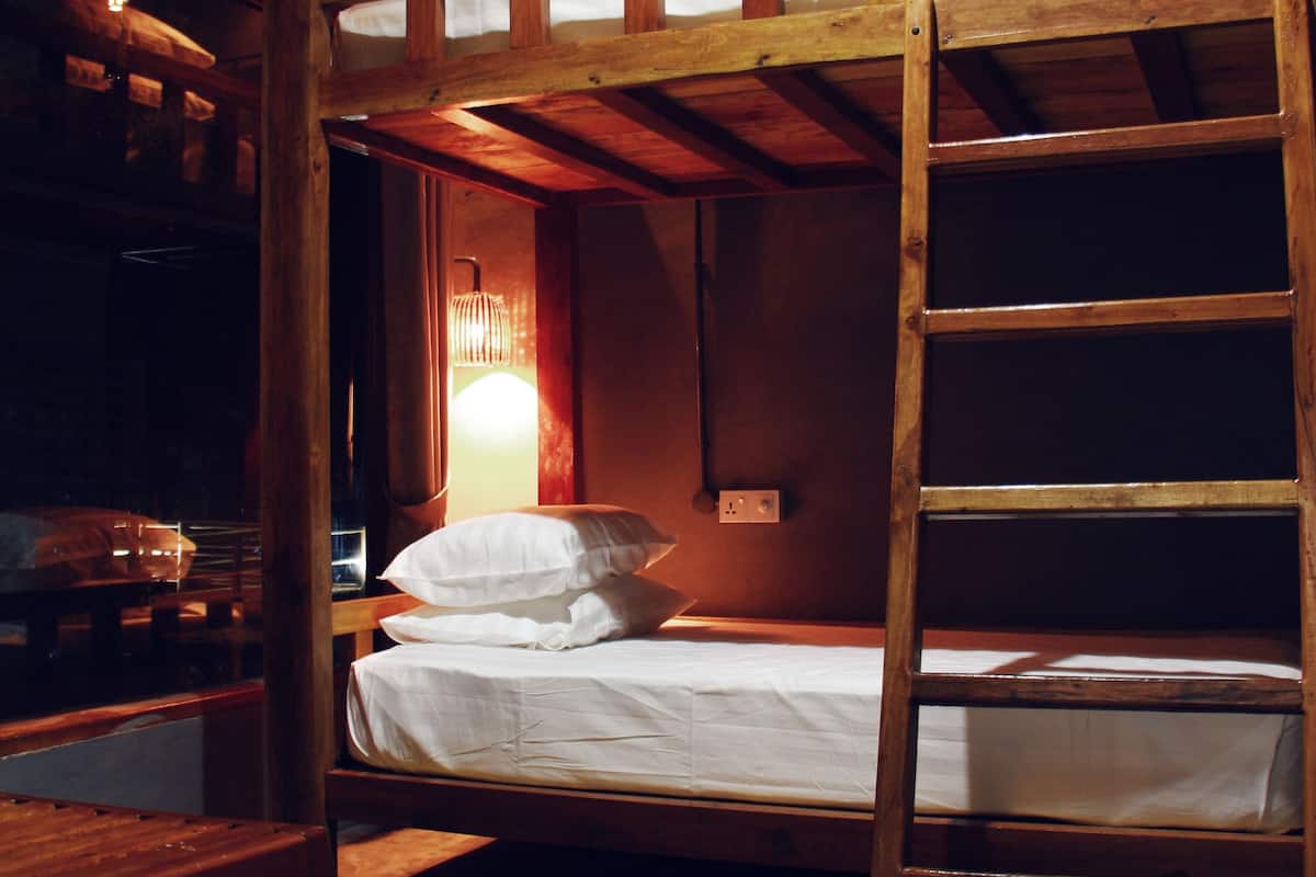 A bunk bed with a wooden ladder, a bedside lamp, and a window with curtains.