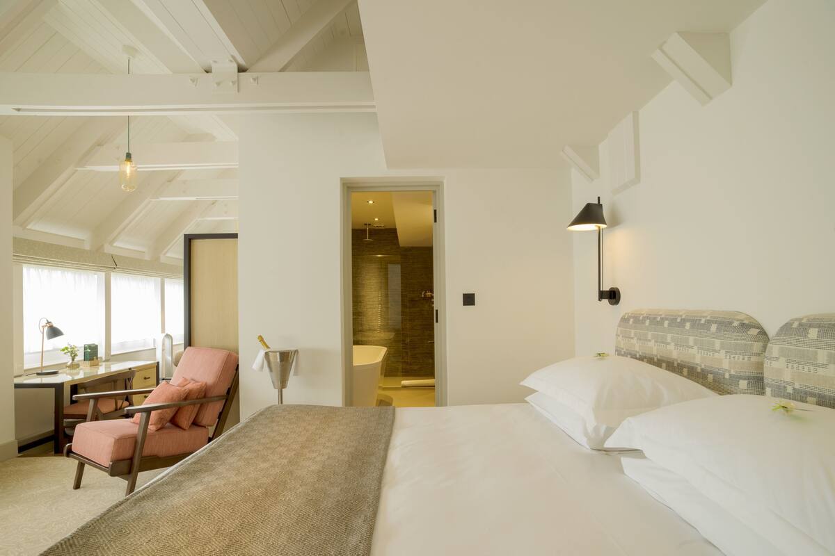 Une chambre d’hôtel avec un lit, un bureau, une chaise et une salle de bain visible à travers une porte ouverte.