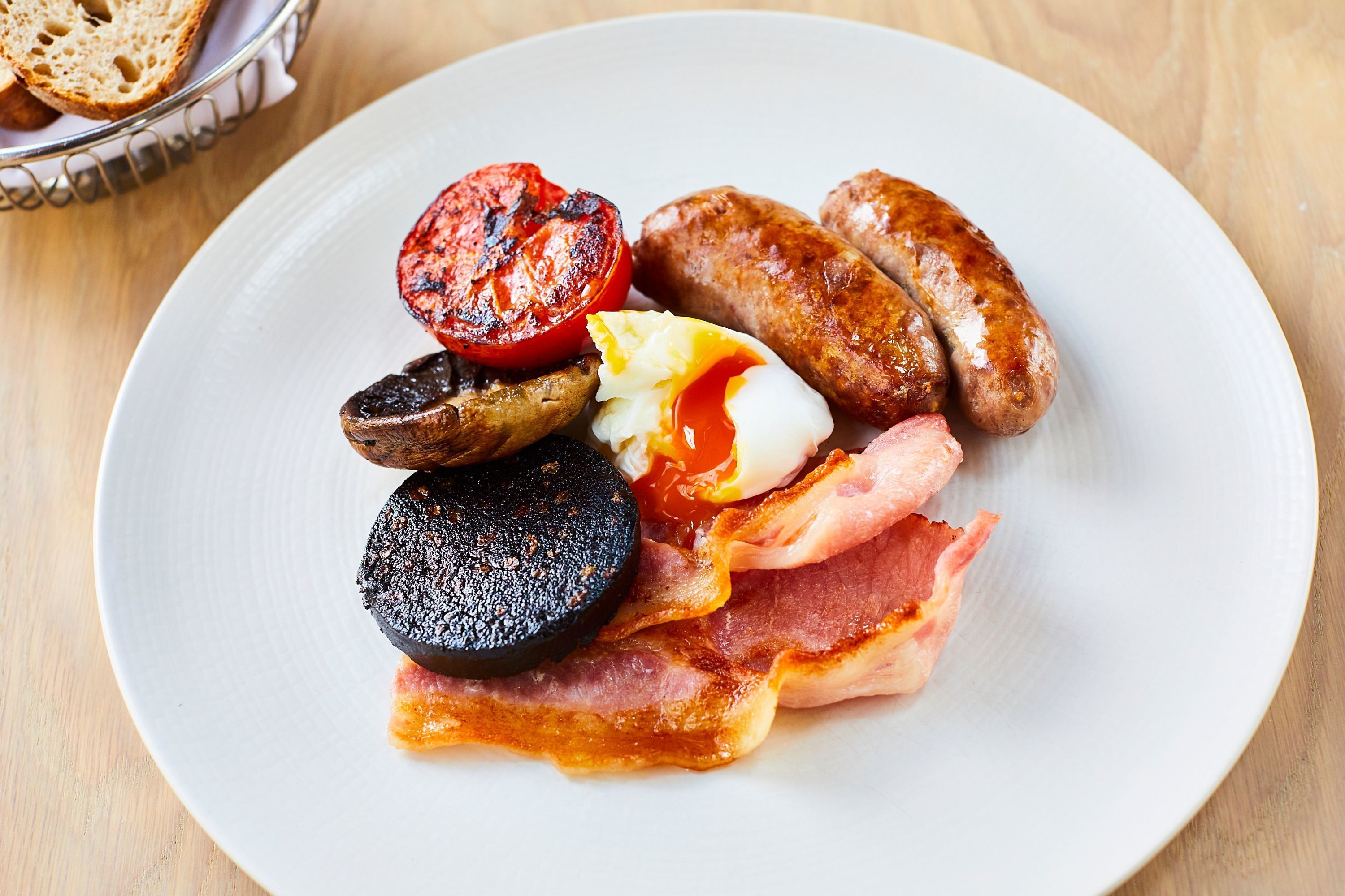A plate of breakfast food including sausages, bacon, eggs, and a grilled tomato.