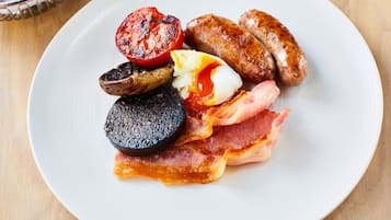 Prato com café da manhã incluindo linguiça, bacon, ovos e tomate grelhado.