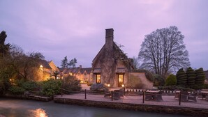 A rustic building with a thatched roof, surrounded by a water body and outdoor seating area. - Old Swan & Minster Mill Hotel (Witney)