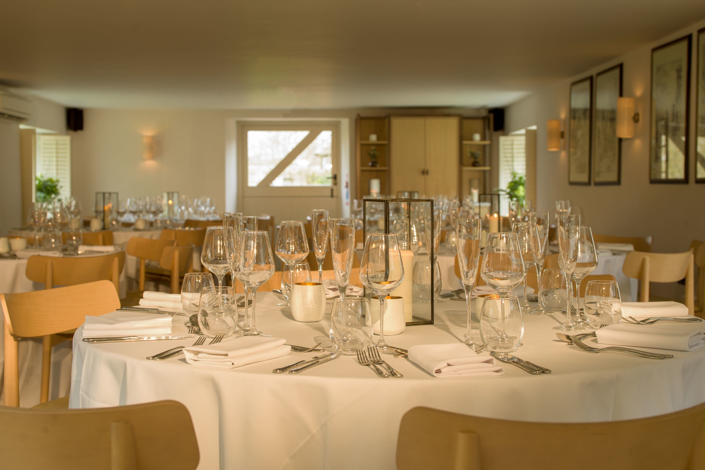 A dining area with round tables set for a formal event, featuring white tablecloths, glassware, and candles.