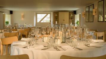 A dining area with round tables set for a formal event, featuring white tablecloths, glassware, and candles.
