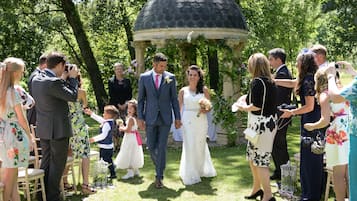Una ceremonia de boda en un jardín con un pabellón, invitados y una novia y un novio.