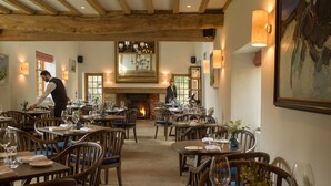 A restaurant with wooden beams, tables set for dining, and a fireplace in the background. - Old Swan & Minster Mill Hotel (Witney)