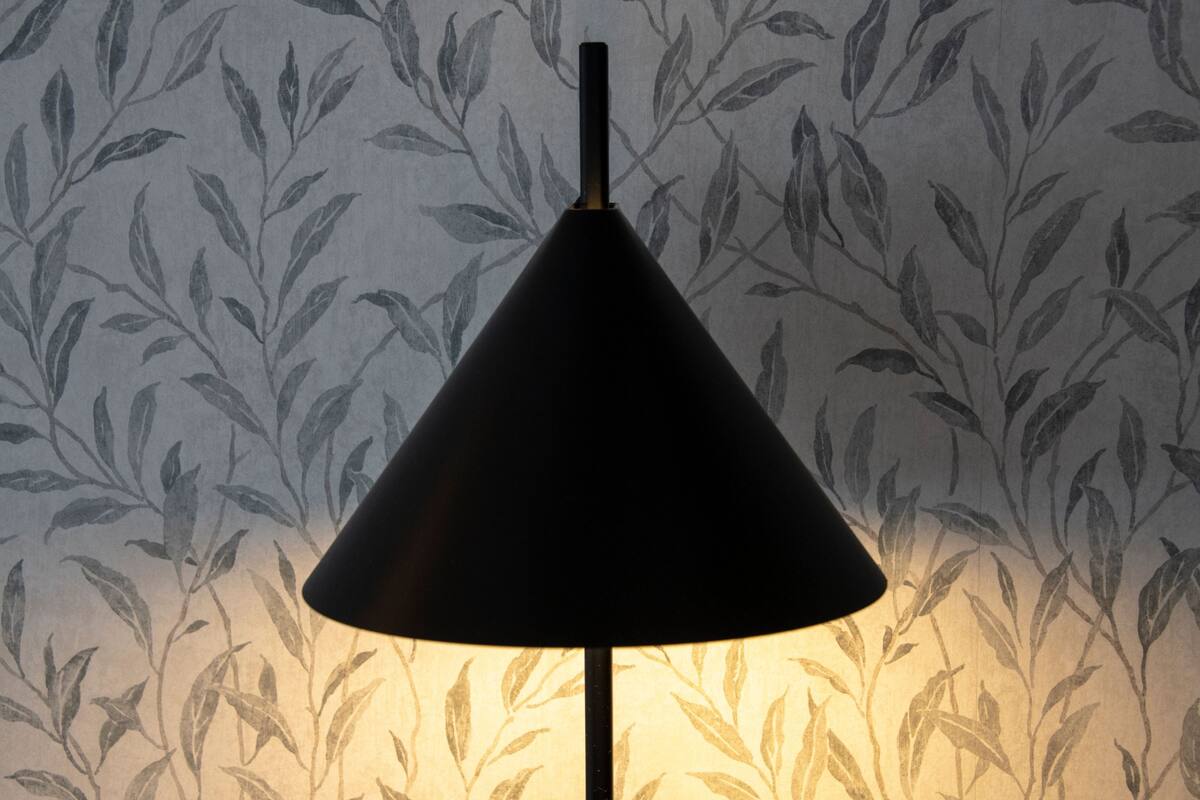 Une lampe dotée d’un abat-jour conique, placée devant un papier peint orné d’un motif de feuilles.