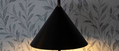 A lamp with a conical shade against a wallpaper with a leaf pattern.