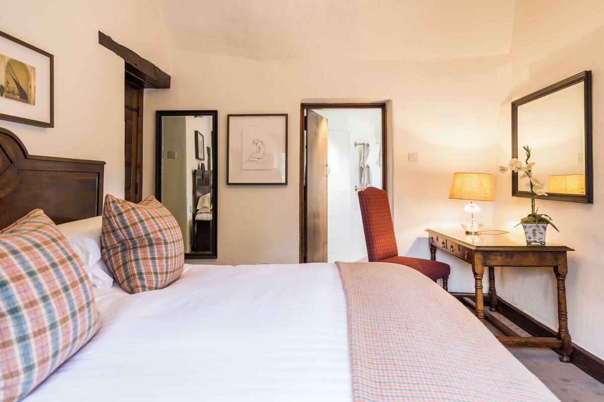 Une chambre d’hôtel avec un grand lit, un bureau en bois, une chaise, un miroir et un tableau encadré au mur.