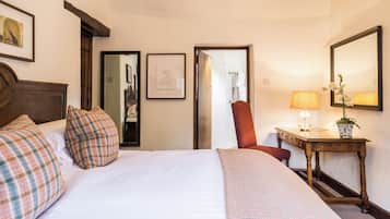 Quarto de hotel com uma cama grande, uma escrivaninha de madeira, uma cadeira, um espelho e um quadro na parede.