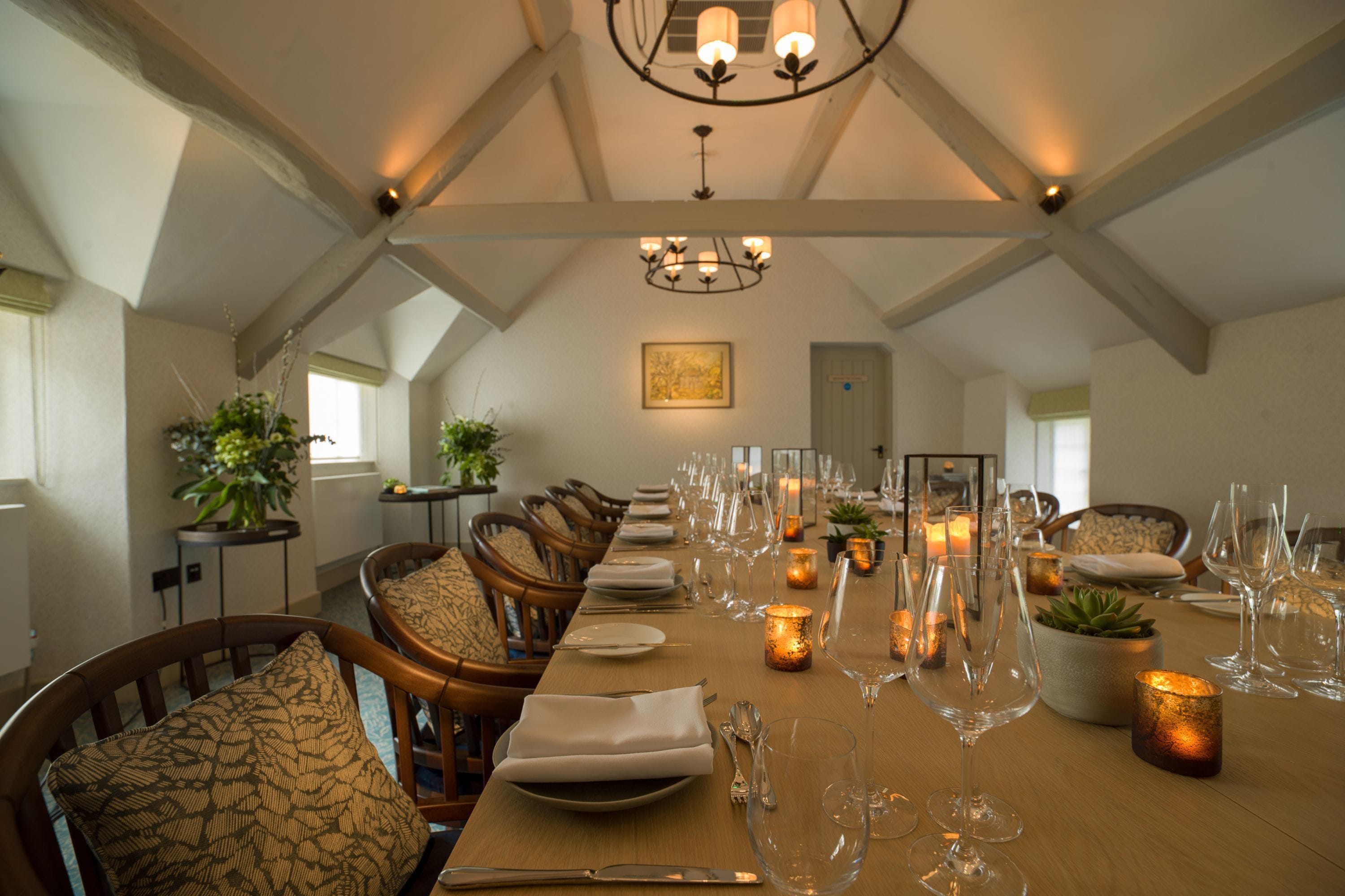Uma sala de jantar com uma mesa comprida posta para refeição, rodeada por cadeiras de madeira com almofadas estampadas.
