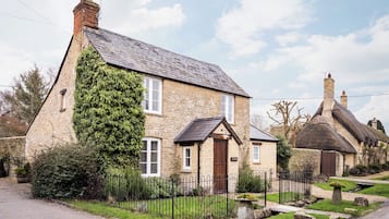 A stone house with ivy-covered walls, a thatched roof, and a traditional English countryside setting.