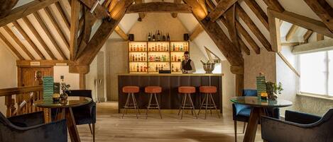 A bar area with wooden beams, a glass table, and bar stools. There is a shelf with bottles and a sign that reads "THE DAY".