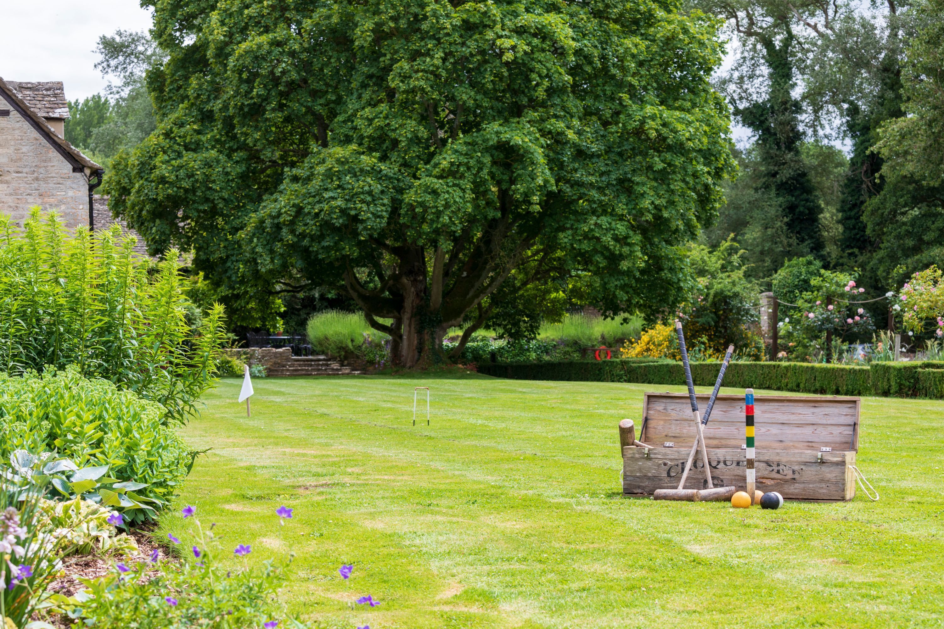 A well-maintained garden with a large tree, a wooden bench, and croquet equipment.