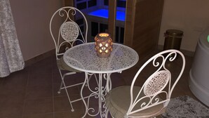 Een ronde metalen tafel met een kandelaar in het midden, omringd door vier metalen stoelen met gedetailleerde versieringen.