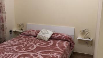 A neatly made bed with a patterned bedspread, two bedside tables with lamps, and a wall decoration of pink roses.