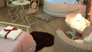 Een spa ruimte met een grote wanddecoratie van een waterval, een jacuzzi, een houten sauna en een knus zithoekje met een tafel en stoelen.