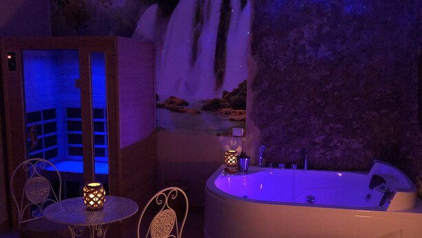 Een wellnessruimte met een wanddecoratie van een waterval, een rond bad en twee sierlijke stoelen.