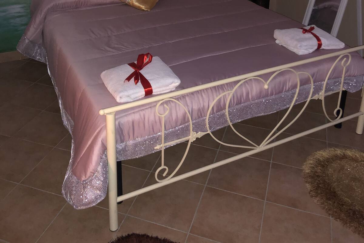 A bed with a tufted headboard, a purple bedspread, and two towels with red ribbons.