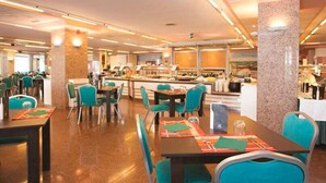 A spacious dining area with multiple tables and chairs, a central buffet, and a kitchen area in the background. - Apartamentos Esmeralda (Calpe)