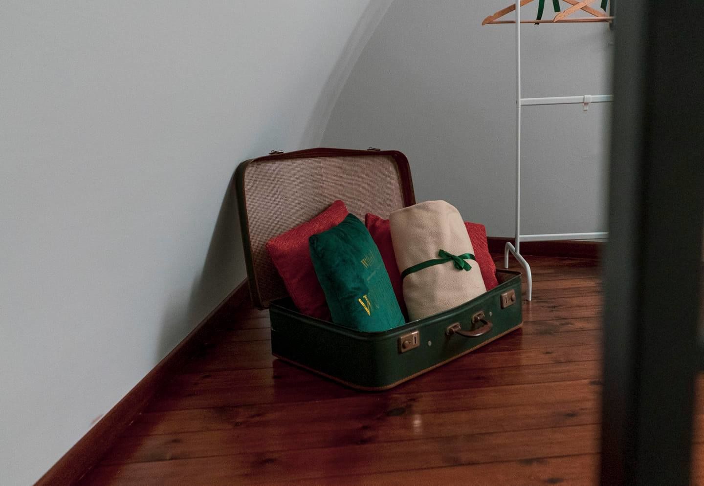 Una valigia verde su un pavimento di legno, con una parete bianca sullo sfondo.