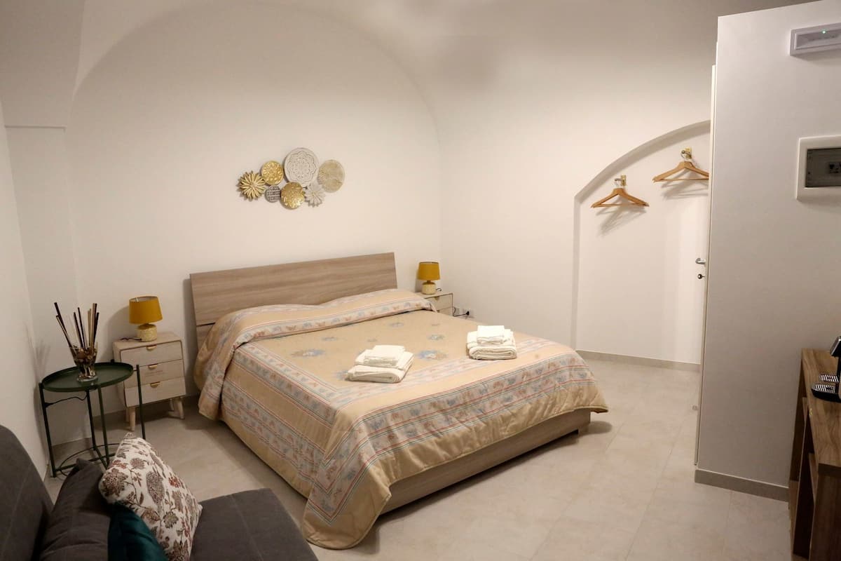 A bedroom with a bed, bedside tables, a lamp, a small table with a decorative item, and a coat rack with hangers.