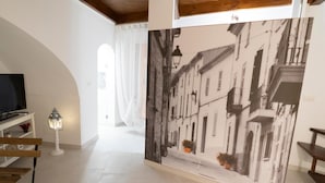 A hallway with a large black and white photograph of a street scene, a television, a small table with a lamp, and a bench. - Il Vicolo B&B (Putignano)
