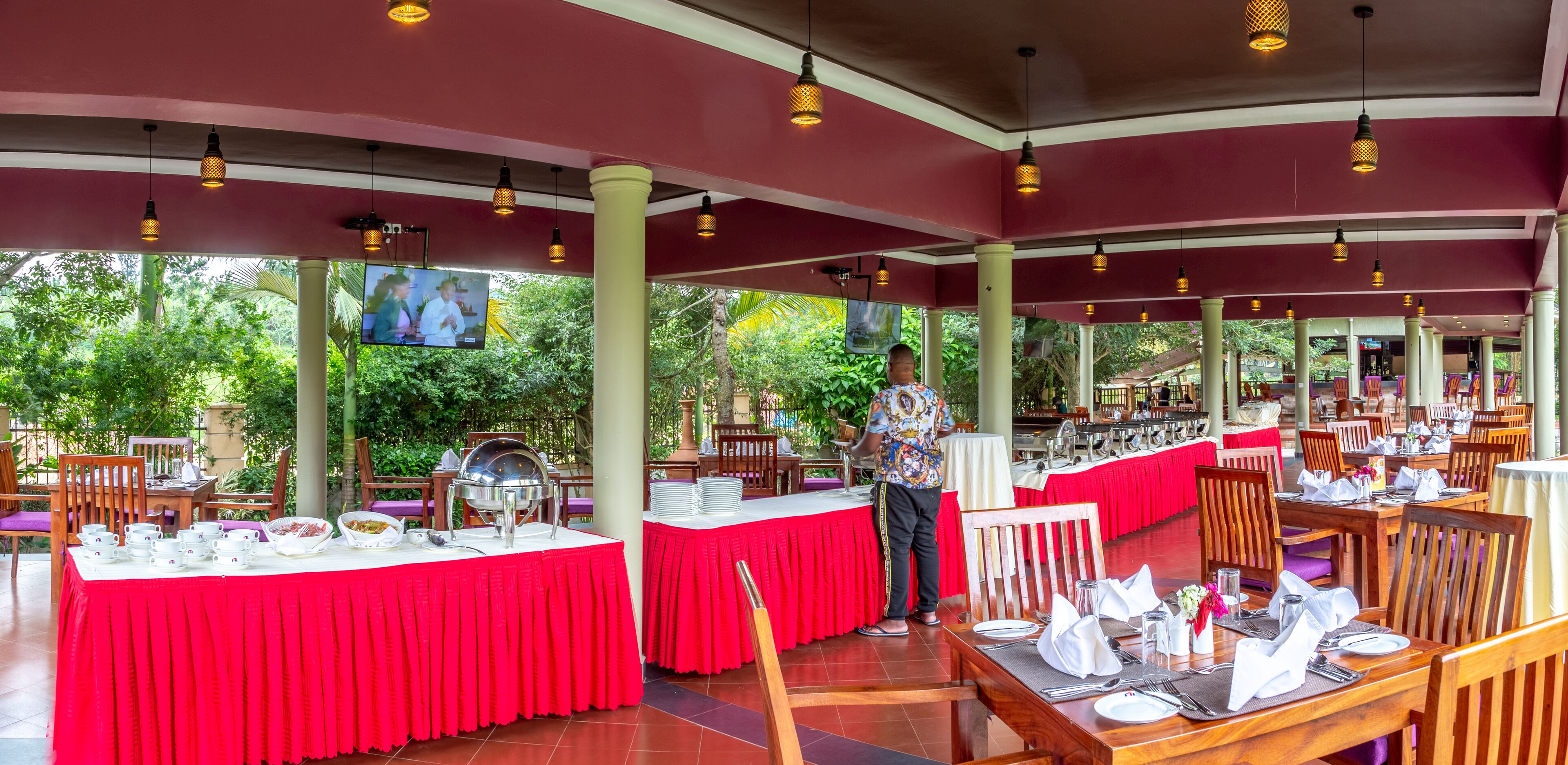A restaurant with red tablecloths, wooden chairs, and hanging pendant lights.