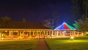 A covered outdoor seating area with tables and chairs, a pathway, and a building with a roof. - Nyaika Hotel (Fort Portal)