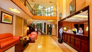 A hotel lobby with a reception desk, a staircase, and a seating area with a sofa and a coffee table. - Nyaika Hotel (Fort Portal)