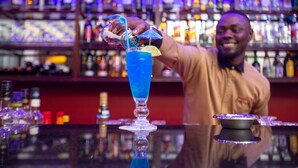 A bartender preparing a blue cocktail with a lemon twist on a bar counter. - Nyaika Hotel (Fort Portal)