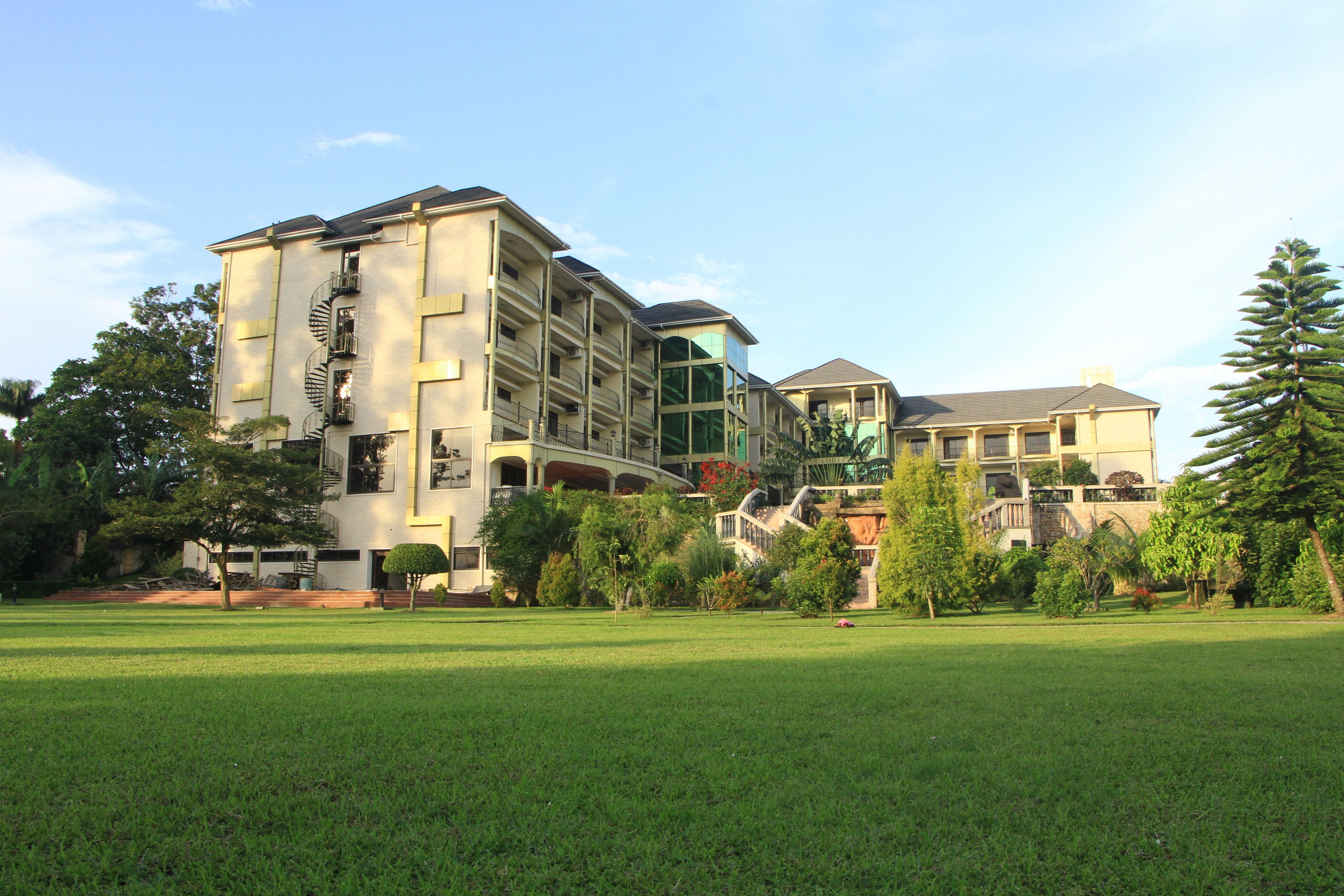 A multi-story hotel with a spiral staircase, a large glass facade, and a well-maintained lawn.