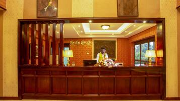A reception desk with a wooden panel design, a receptionist, and a decorative wall with city names.