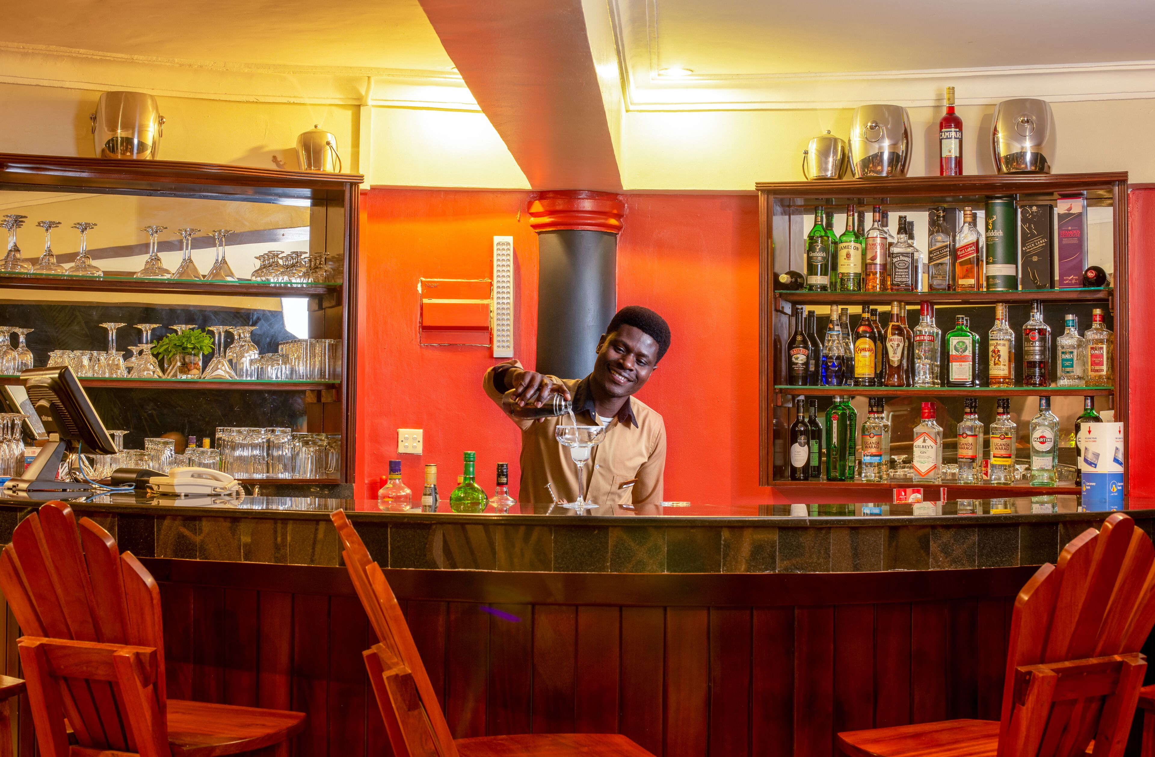A bar area with a bartender, shelves of liquor bottles, and a bar counter.