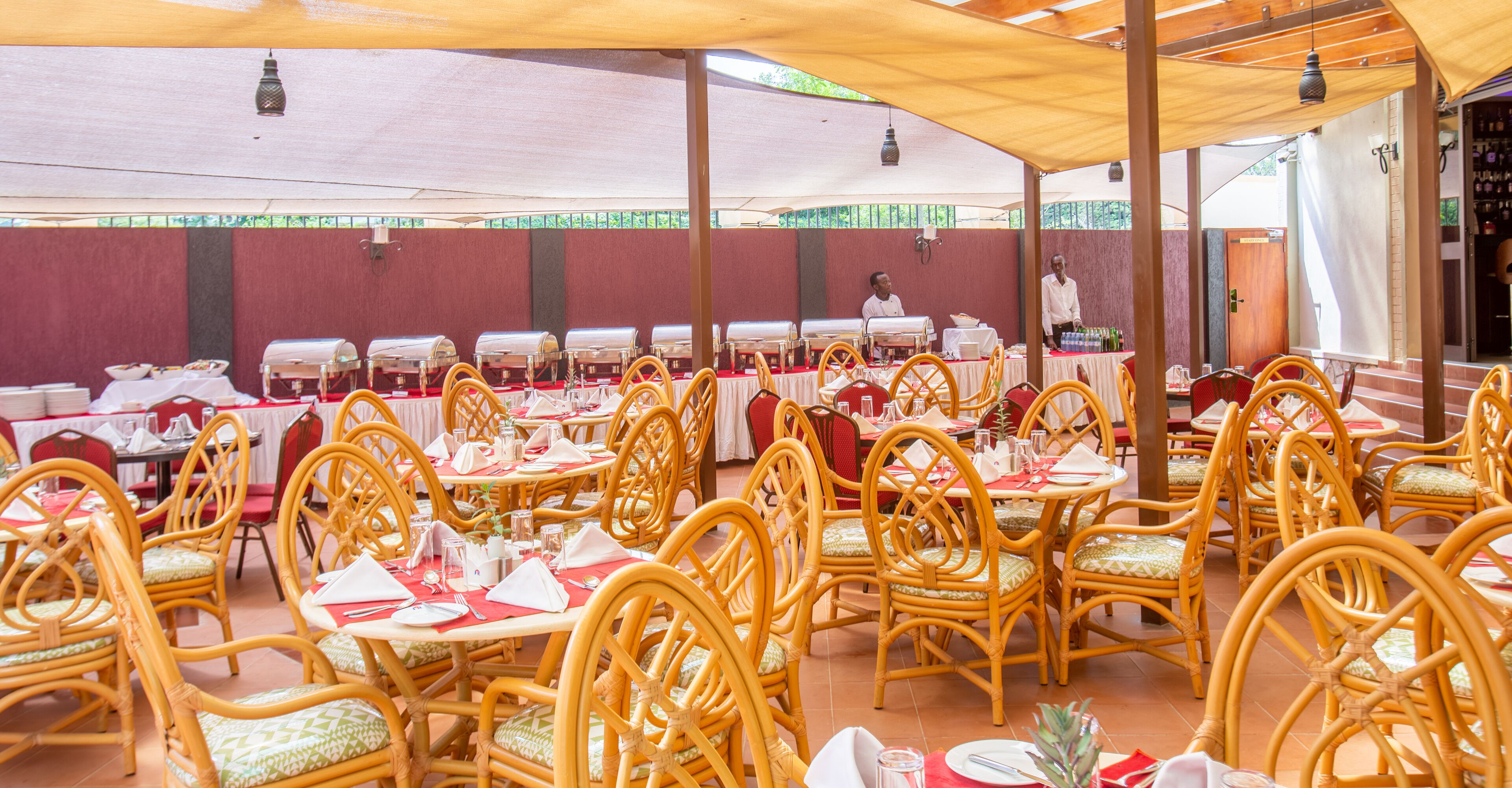 A covered outdoor dining area with wicker chairs and tables set for a meal.