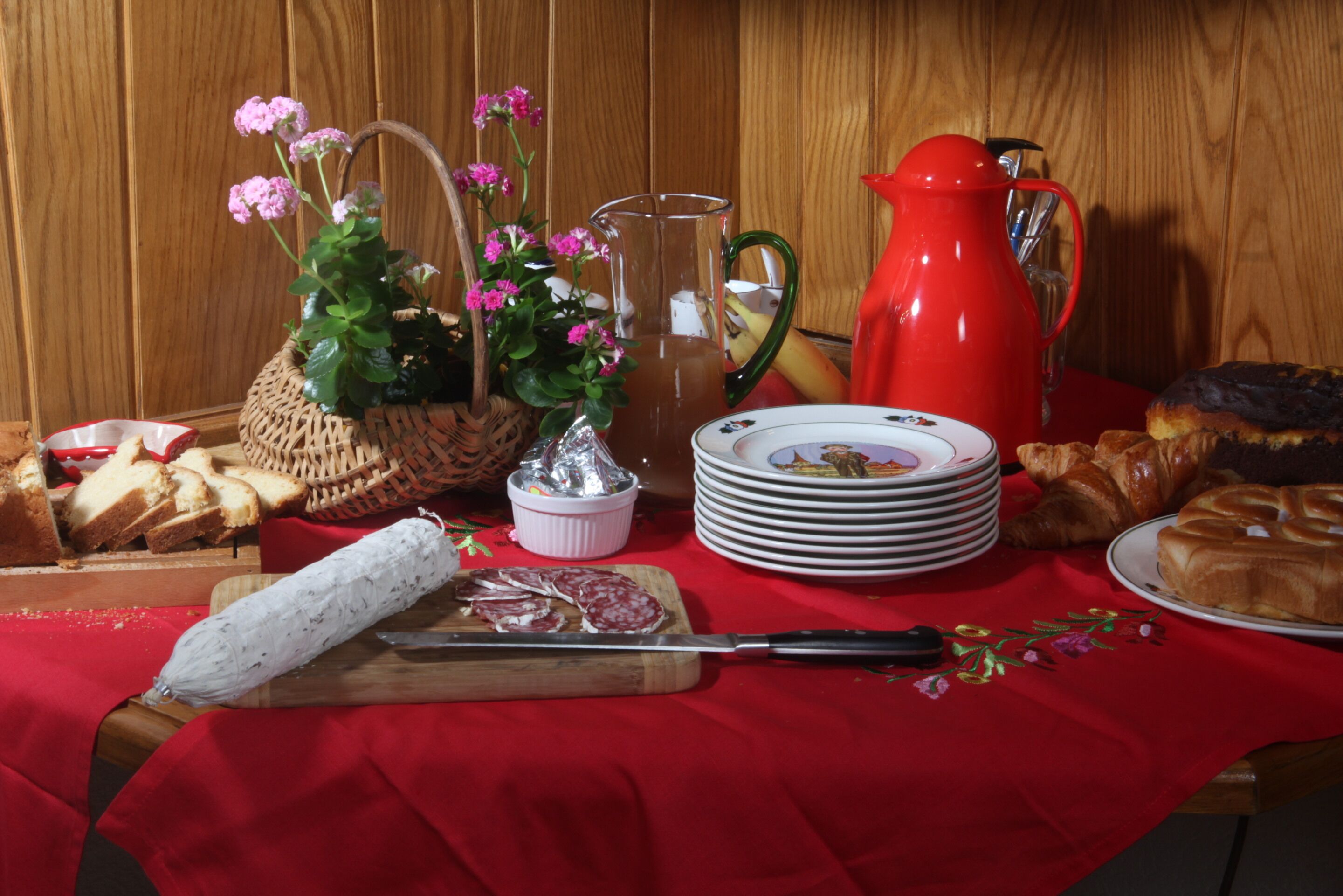 Une table avec des aliments, une carafe, un panier de fleurs et un couteau.