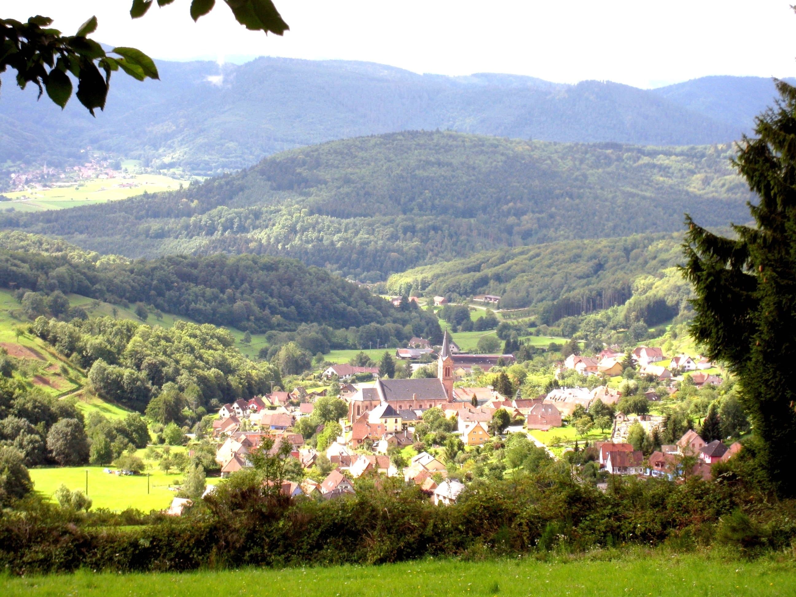 A rural village with a church and residential buildings surrounded by green hills.