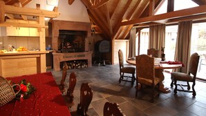 Un intérieur rustique avec un plafond en bois, une cheminée, un coin repas avec des chaises et une cuisine dotée d’un comptoir en bois.