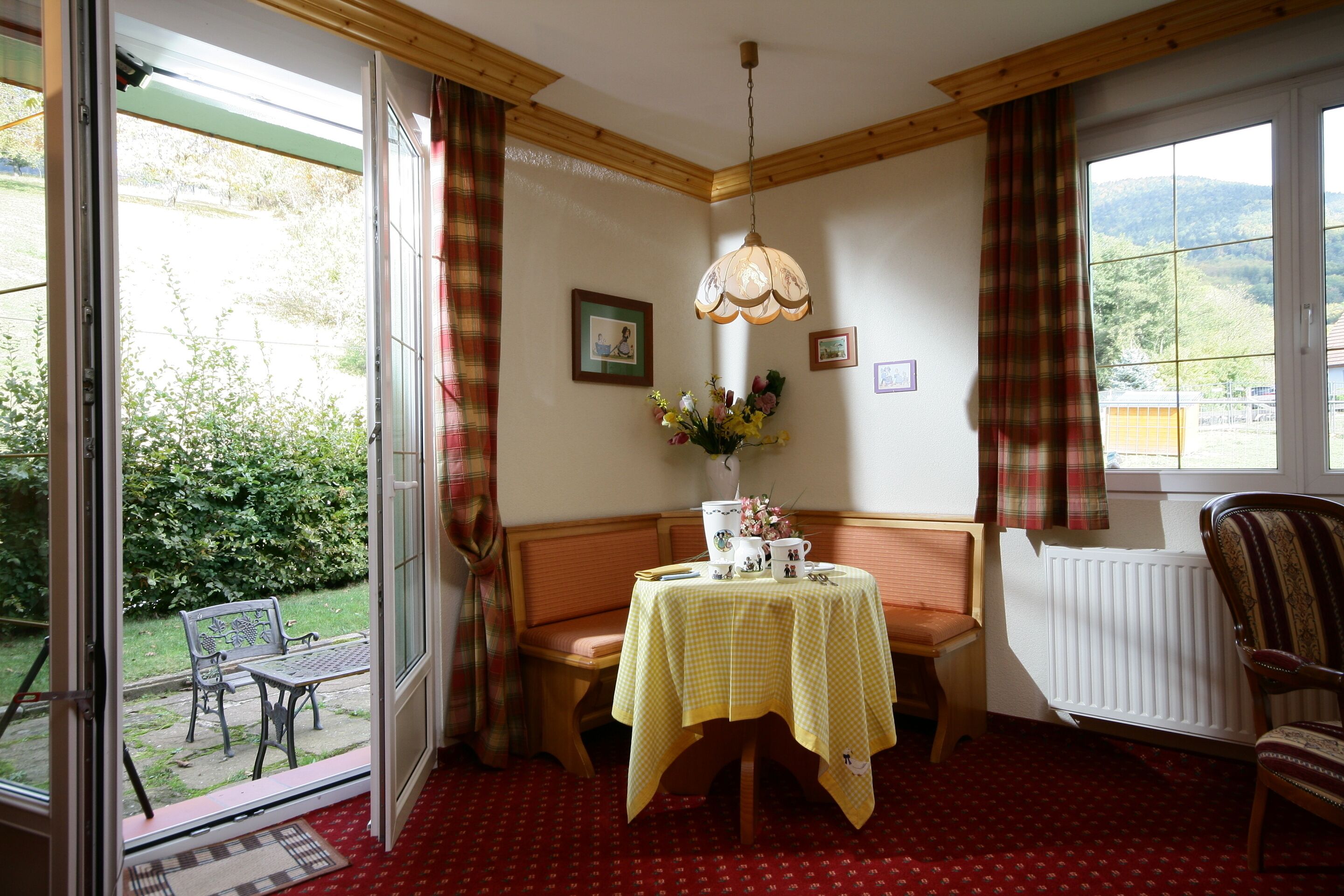 A room with a table set for two, a bench, a radiator, and a window with a view of greenery.