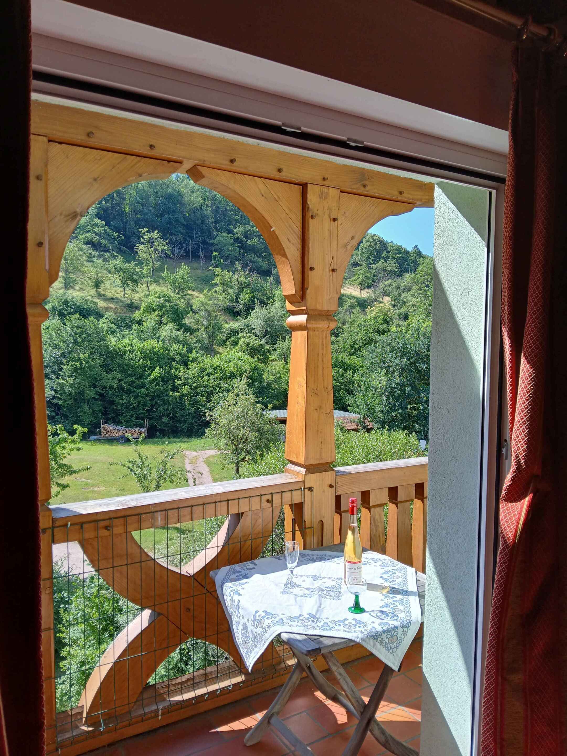 Een balkon met een tafel, een fles en een glas, met uitzicht op een groen landschap.