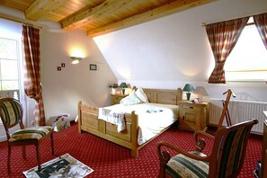 Quarto com cama de madeira, duas cadeiras, mesa de cabeceira e janela com cortinas.