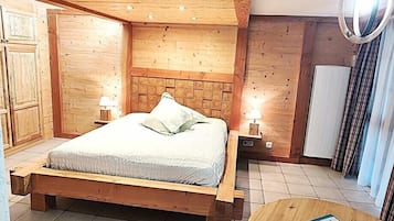 A wooden bedroom with a bed, bedside lamps, and a round wooden table with a certificate.