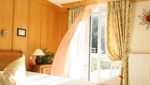 Une chambre à coucher avec un lit en bois, une table de chevet avec une lampe, une plante en pot et une vue à travers une porte vitrée.