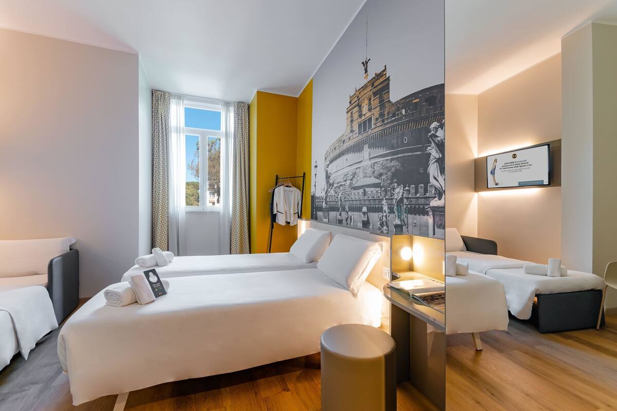 Una habitación de hotel moderna con una cama grande, un escritorio y una silla. Cuenta con una ventana con cortinas, una obra de arte colgada en la pared y un certificado enmarcado.