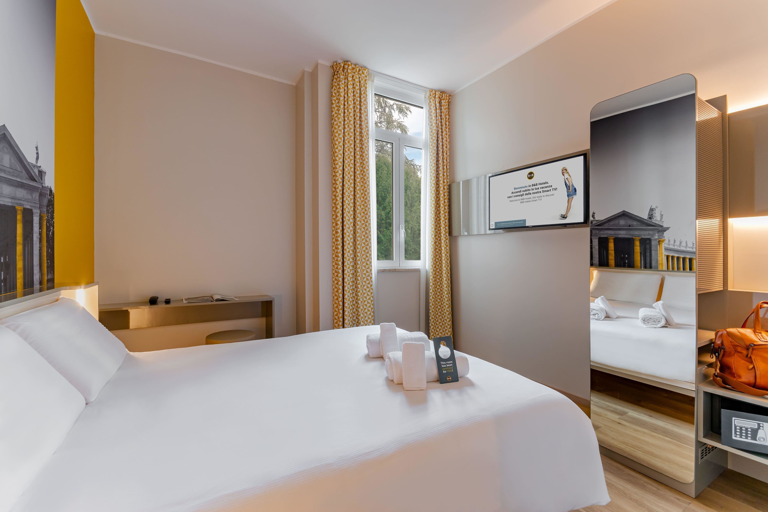 Ein Hotelzimmer mit einem großen Bett, einem Schreibtisch, einem Sessel, einem Fernseher und einem Spiegel.