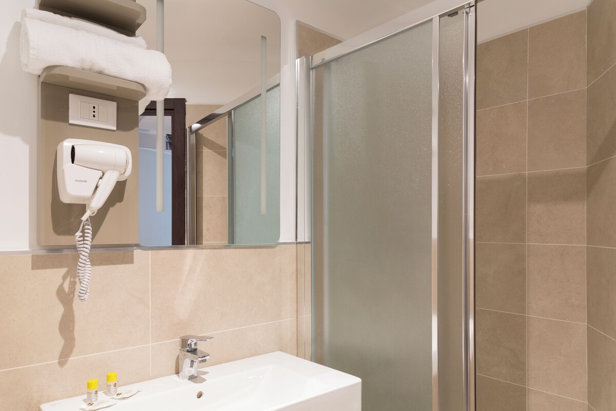 A bathroom with a white sink, a hairdryer mounted on the wall, and a glass shower enclosure.