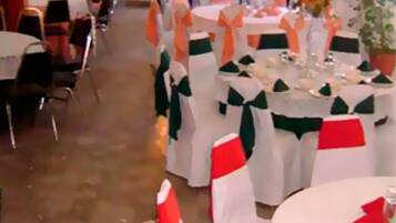 A banquet hall with round tables, each adorned with white tablecloths and green sashes.