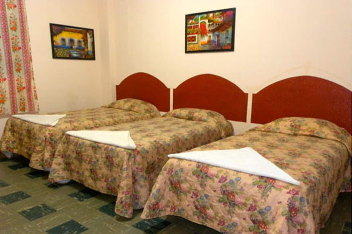 A room with three single beds with floral bedding, a red headboard, and two framed artworks on the wall.